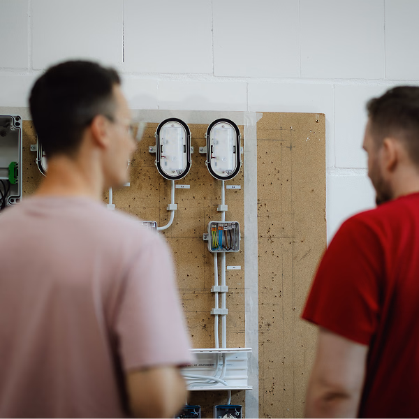 Zwei Männer von hinten begutachten elektrische Installationen an einem Board
